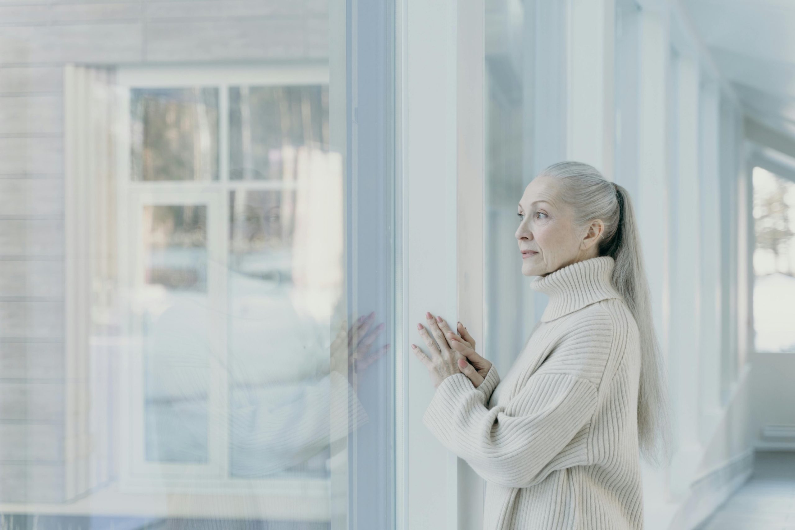 A woman in a house looks outside through a large window.